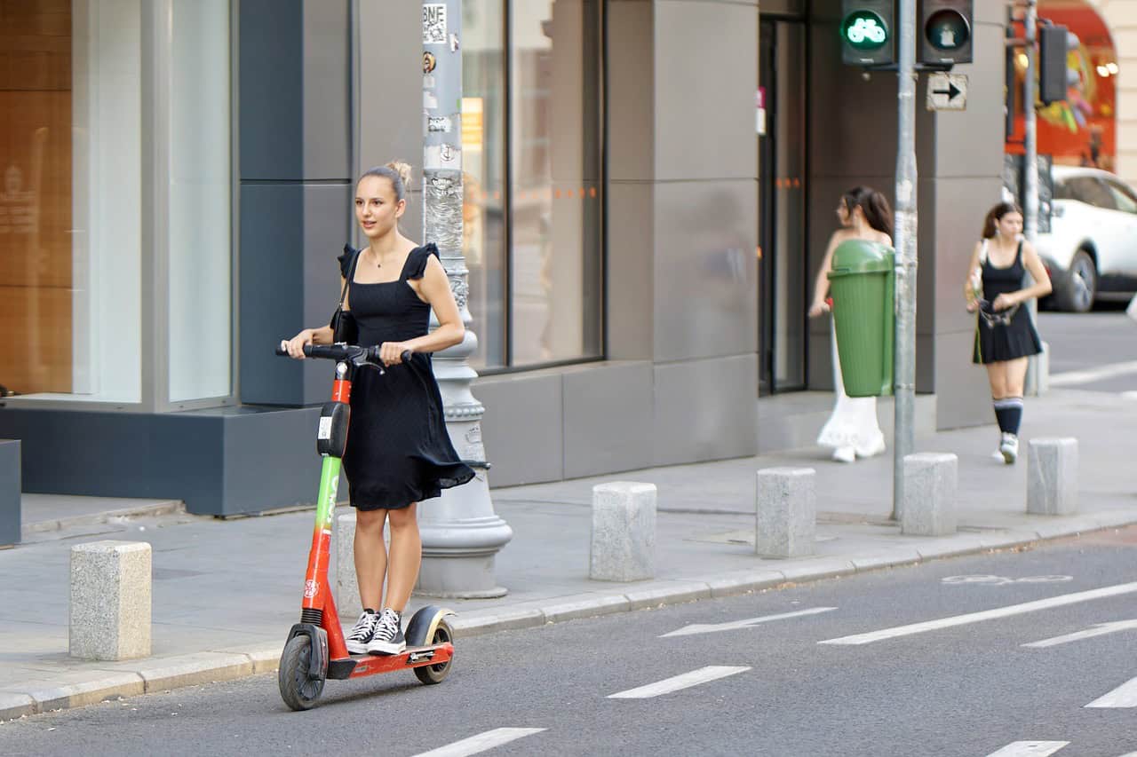 Girl in black dress ride rented e-scooter on a bike path